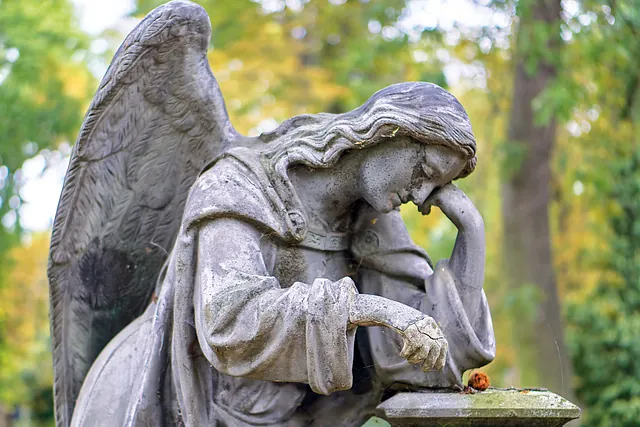 Traurige Engelstatue mit Bäumen im Hintergrund